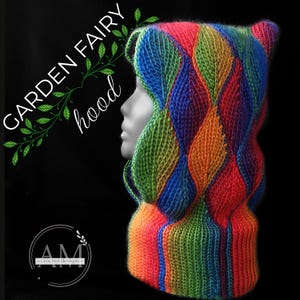 May include: A colorful crocheted hooded scarf with a leafy pattern in shades of green, blue, orange, and red. The hood is pulled up and the scarf is worn on a mannequin. The text "GARDEN FAIRY hood" is visible above the scarf.