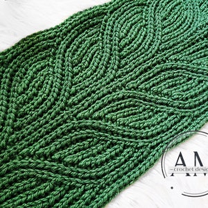 Może przedstawiać: Zielony szalik robiony na szydełku z powtarzającym się wzorem liści. Szalik jest wykonany z grubego włóczki i ma fakturowany wygląd.