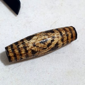 Pode incluir: Uma conta de olho de tigre marrom e preto com um padrão listrado. A conta é lisa e polida.