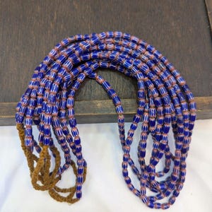 May include: A strand of blue and white glass beads with a brown cord. The beads are cylindrical and have a striped pattern.