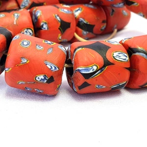 May include: A close-up of a string of red, black, and blue glass beads. The beads are cylindrical and have a mottled, textured surface.
