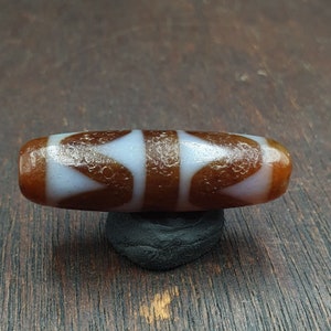 May include: A brown and white agate bead with a geometric pattern. The bead is smooth and polished, and it has a natural, earthy look.