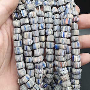 Puede incluir: Una hebra de cuentas de vidrio de colores con un patrón a rayas. Las cuentas son una mezcla de azul, blanco y rojo.