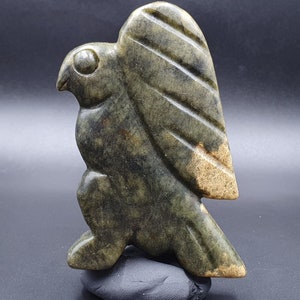 May include: A green and gold jade carving of a bird with outstretched wings. The bird is perched on a black base.