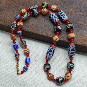 May include: A necklace made of colorful glass beads with intricate patterns. The beads are red, blue, black, and white with gold accents. The necklace is strung on a red cord.