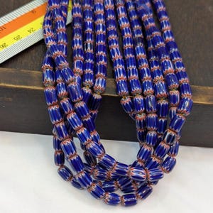 May include: A strand of blue and white glass beads with red accents. The beads are cylindrical and have a striped pattern.