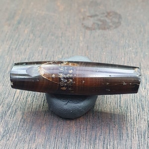 May include: A dark brown and black banded agate bead with a polished finish. The bead has a natural, organic shape and is approximately 5 cm long.