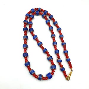 May include: A necklace made of blue and red glass beads. The beads are arranged in an alternating pattern. The necklace has a gold clasp.