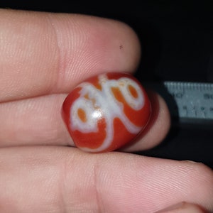 May include: A red carnelian bead with a white swirl design. The bead is approximately 2.5 cm in diameter.
