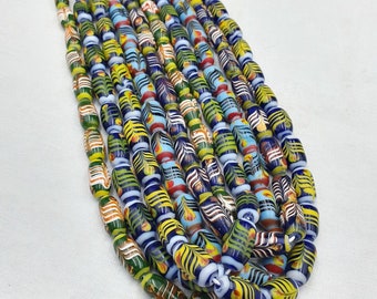 May include: A strand of colorful glass beads with intricate patterns. The beads are blue, green, yellow, and white with a variety of designs. The beads are strung together on a white cord.