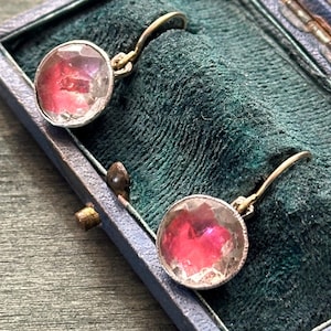 May include: A pair of antique earrings with pink glass stones set in gold tone metal. The earrings are in a blue velvet jewellery box.