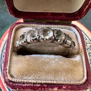 May include: A silver ring with six clear stones set in a row. The ring is in a red velvet box.