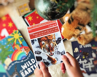 Può includere: Mani di bambino che tengono una carta con una tigre e la scritta "In pericolo". Sono visibili altre carte e una tigre di peluche. La carta dice "Wild Earth" e include informazioni sull'animale.