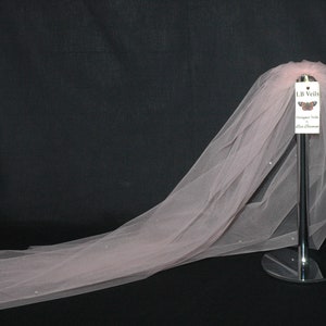 May include: A blush pink tulle wedding veil with a small tag that reads "LB Veils Designer Veils Made in Oklahoma".