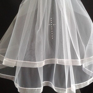 May include: White tulle veil with two layers of satin ribbon trim and a rhinestone cross embellishment.