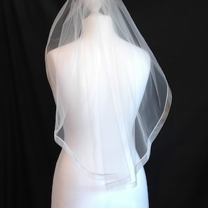 May include: A white bridal veil with a satin edge. The veil is on a white mannequin head.