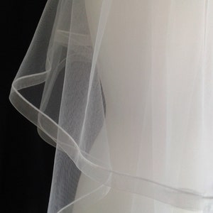 May include: A white single-tier bridal veil with a scalloped edge. The veil is made of soft tulle and is designed to be worn over the face.