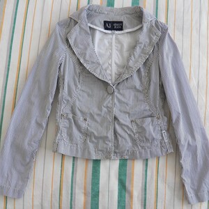 May include: A striped blazer with a white collar and a button closure. The blazer has a small pocket on the left side and a label that reads "A|X Armani Jeans".