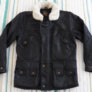 May include: A black leather jacket with a faux fur collar. The jacket has multiple pockets and a button closure. The label on the jacket reads "Country Leather".