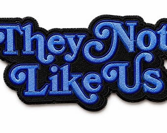 May include: A black embroidered patch with the words "They Not Like Us" in blue, stylized lettering. The patch has a black border and a textured appearance, suitable for application on clothing or accessories.