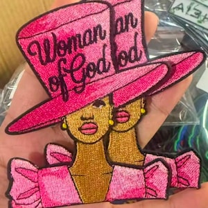 May include: Pink embroidered iron-on patch featuring a woman wearing a pink hat with the text "Woman of God" on it.