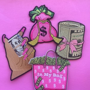May include: Four embroidered iron-on patches featuring a pink money bag, a roll of cash with a pink bow, a hand holding a dollar bill, and a pink tote bag with the text "In My Bag" and dollar signs.