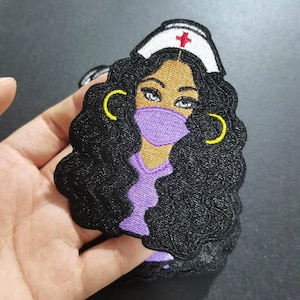 May include: Embroidered iron-on patch featuring a cartoon illustration of a Black woman with curly hair wearing a purple medical scrub top, a white nurse's cap with a red cross, and a purple face mask. She has yellow hoop earrings.