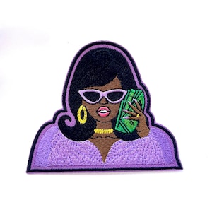 May include: An embroidered iron-on patch featuring a cartoon woman with black hair, wearing sunglasses and a purple dress, holding a stack of money to her ear like a phone.