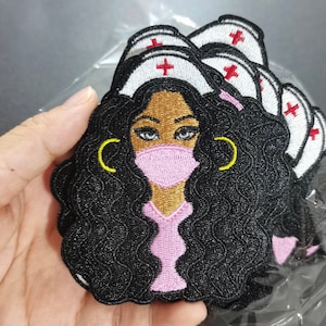 May include: A set of embroidered iron-on patches featuring a black woman with curly hair wearing a white nurse's cap, a pink face mask, and a pink scrub top. The patches have a red cross on the cap and yellow hoop earrings.
