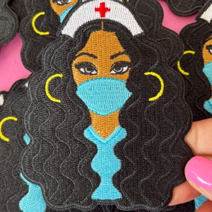 May include: Black and brown embroidered iron-on patch of a woman with curly black hair wearing a blue medical uniform, a white nurse's cap with a red cross, and a blue face mask.