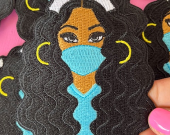 May include: Black and brown embroidered iron-on patch of a woman with curly black hair wearing a blue medical uniform, a white nurse's cap with a red cross, and a blue face mask.