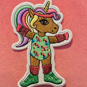 May include: An embroidered iron-on patch featuring a cartoon unicorn wearing a pink headband, green and blue workout outfit, and red wrist warmers. The unicorn has a gold horn and a pink, purple, and green mane.