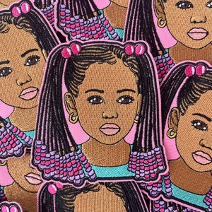 May include: Embroidered patch featuring a young girl with brown skin, black braids, and pink and purple accents. The patch has a pink border and a turquoise top. The girl is wearing gold hoop earrings.