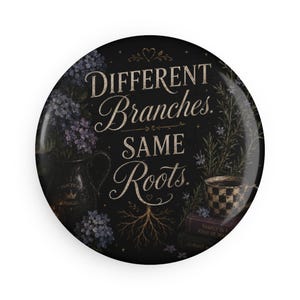 May include: A round pin-back button with a black background featuring the text "Different Branches. Same Roots." in a decorative font. The design includes illustrations of purple flowers in a pitcher, a checkered teacup, and stacked books.