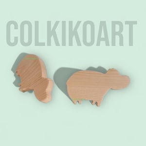 Puede incluir: Dos recortes de animales de madera, un león y un hipopótamo, se muestran sobre un fondo verde claro. El león está a la izquierda y el hipopótamo a la derecha. El texto "COLKIKOART" está en la parte superior y "Only on Etsy" en la inferior.