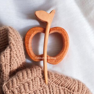 May include: A wooden apple-shaped hair pin with a long stem. The pin is made of natural wood and has a warm brown color.