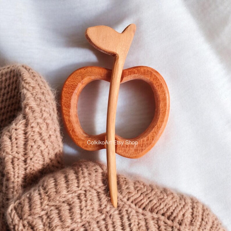 May include: A wooden apple-shaped hair pin with a long stem. The pin is made of natural wood and has a warm brown color.