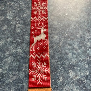 May include: A red leather bracelet with a white reindeer and snowflake design.