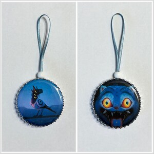 May include: Two round ornaments with blue and silver trim. One features a blue bird with a hat, the other a blue cat with yellow eyes. Each has a blue ribbon for hanging.