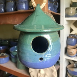 May include: A blue and green ceramic birdhouse with a small hole for birds to enter. The birdhouse is hanging from a string.