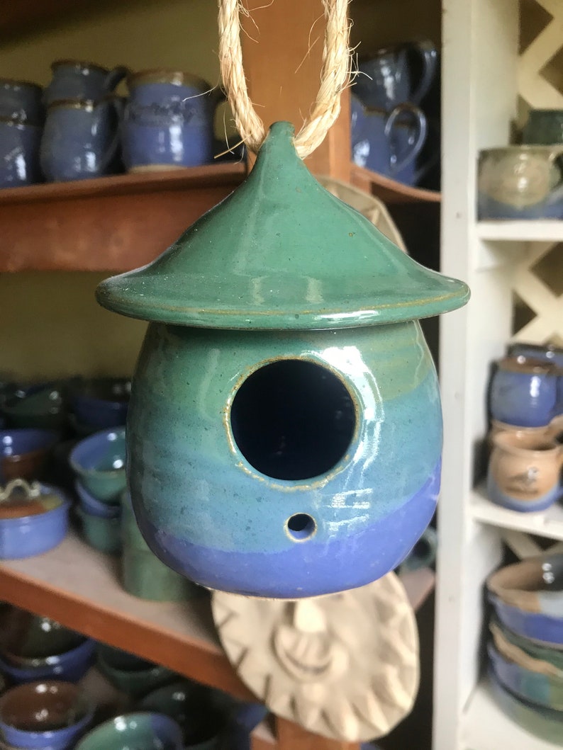 May include: A blue and green ceramic birdhouse with a small hole for birds to enter. The birdhouse is hanging from a string.