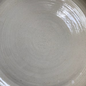 May include: A white ceramic plate with a smooth, glossy finish. The plate has a slightly raised rim and a circular shape.