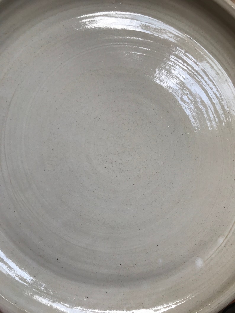 May include: A white ceramic plate with a smooth, glossy finish. The plate has a slightly raised rim and a circular shape.