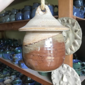 May include: A brown and white ceramic jar with a lid and a rope handle. The jar has a speckled glaze and a brown and white swirl design.