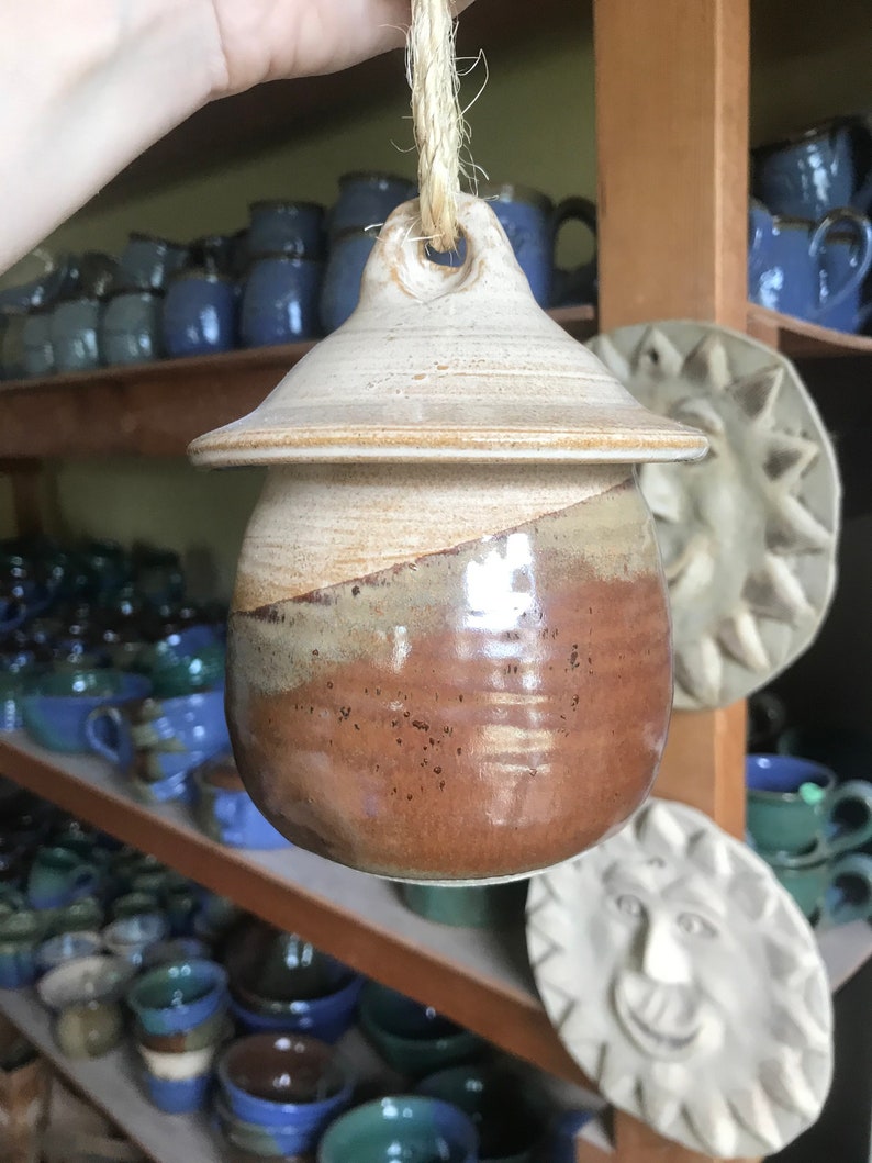 May include: A brown and white ceramic jar with a lid and a rope handle. The jar has a speckled glaze and a brown and white swirl design.