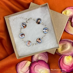 May include: Silver-toned bracelet featuring seven circular charms with portraits, set against a light blue background. The bracelet is displayed in a small, open cardboard box, with rose petals scattered around.