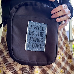 May include: A dark brown canvas crossbody bag with a blue denim patch that says "I will do the things I love".
