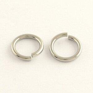 May include: Two silver-coloured, open jump rings. Each ring is circular with a small gap, allowing them to be attached to other jewellery components. The rings are made of a shiny, metallic material and are set against a white background.