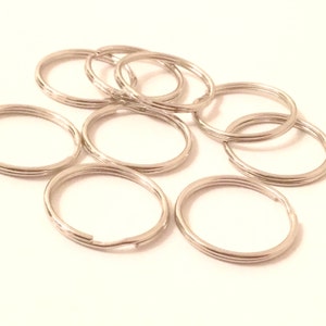 May include: A close-up of a pile of silver key rings. The key rings are all the same size and shape, and they are arranged in a random order.