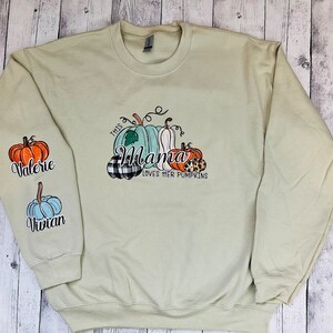Pode incluir: Uma camisa de frio verde claro com o texto "This Mama Loves Her Pumpkins" e um gr&aacute;fico de ab&oacute;boras. As mangas t&ecirc;m os nomes "Valerie" e "Vivian" nelas.